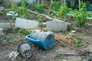 Regadera sucia en el suelo en el patio trasero de la casa con granja de hortalizas borrosa en segundo plano.