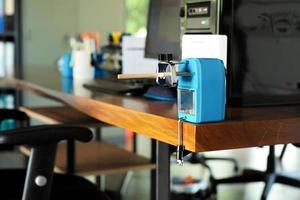 Closeup pencil sharpener with pencil inside installed on the top of wooden table with blurred computer and stationary in background photo