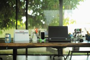 Work from home concept. Closeup laptop on the wooden table surrounded by the office stationaries with blurred background photo