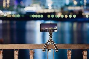 usando un teléfono inteligente en un trípode plegable con larga exposición al mar por la noche foto