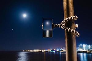 usando un teléfono inteligente en un trípode plegable con larga exposición al mar por la noche foto