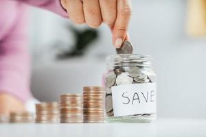 Mano de mujer poniendo moneda de dinero en frasco de vidrio para ahorrar dinero. Ahorro de dinero y concepto financiero.