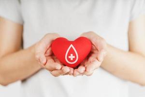 manos de mujer sosteniendo corazón rojo con signo de donante de sangre. concepto de salud, medicina y donación de sangre foto