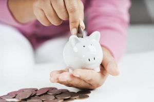 Closeup of business woman hand putting money coin into piggy bank for saving money. saving money and financial concept photo
