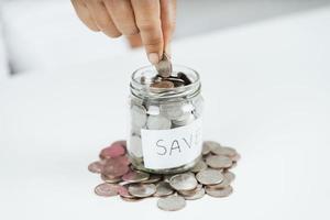 Mano de mujer poniendo moneda de dinero en frasco de vidrio para ahorrar dinero. Ahorro de dinero y concepto financiero. foto