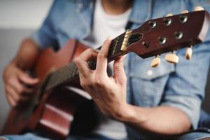 Enjoy handsome asian man practicing or playing the guitar on the sofa at living room photo