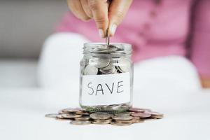 women hand putting money coin into glass jar for saving money. saving money and financial concept photo