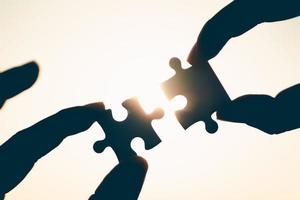 Silhouette of closeup woman and man hand connecting a piece of jigsaw puzzle over sunlight effect. symbol of association and connection concept. business strategy. photo