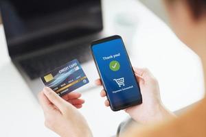 Young woman holding credit card and using smart phone for online shopping, internet banking, e-commerce, spending money, working from home concept photo