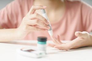 Asian woman using lancet on finger for checking blood sugar level by Glucose meter, Healthcare and Medical, diabetes, glycemia concept photo