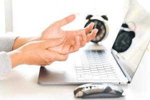 primer plano mujer sosteniendo su dolor en la mano por usar la computadora durante mucho tiempo. concepto de síndrome de oficina. foto