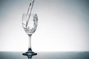 Close up of splash of crystal clear water pouring into the wine glass on the table. photo