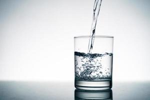 Close up of pouring fresh water into the clear glass from the bottle on table. photo