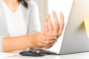 primer plano mujer sosteniendo su dolor en la mano por usar la computadora durante mucho tiempo. concepto de síndrome de oficina. foto