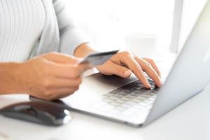 mano de mujer sosteniendo tarjeta de crédito y usando laptop. pago en línea, concepto de compra en línea foto