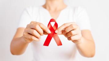 Closeup woman hand holding red ribbon HIV, world AIDS day awareness ribbon. Healthcare and medicine concept.