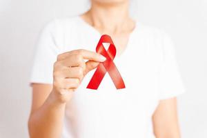 Closeup woman hand holding red ribbon HIV, world AIDS day awareness ribbon. Healthcare and medicine concept. photo