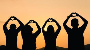 grupo de personas con los brazos levantados y hacer la mano en forma de corazón mirando al amanecer en el fondo de la montaña. conceptos de felicidad, éxito, amistad y comunidad. foto