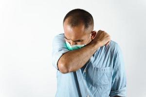 Man wearing face mask sneezing or coughing in his elbow to prevent spread the virus COVID-19 or Corona Virus on white background. photo