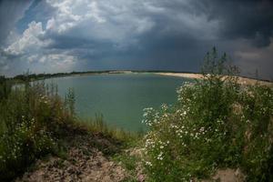 Panorama of a blue lake with a sandy shore. Lake view. Overcast sky.