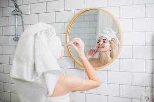 Young woman in white towel apply moisturising oil on face skin. photo