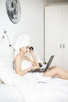 Young woman working in white bed using laptop. photo