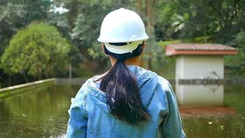 ecologista feminina com chapéu de segurança trabalhando e controlando a qualidade da água na estação de tratamento de águas residuais. engenheiros ambientais trabalhando em usina de reciclagem de água para reutilização. video