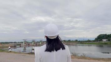 Female engineer in a white helmet reading data in a blueprint and using radio communication at the dam construction site to generate electricity. Clean energy and Technology concepts. video