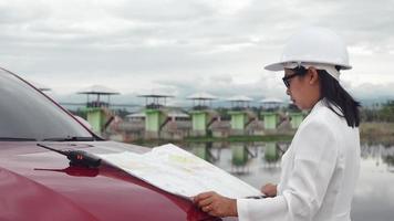 ingeniera con un casco blanco leyendo datos en un plano y usando comunicación por radio en el sitio de construcción de la presa para generar electricidad. conceptos de energía y tecnología limpias. video