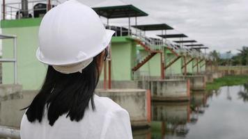 engenheira em um capacete branco, trabalhando com um tablet digital e olhando para o local de construção da barragem para gerar eletricidade. video
