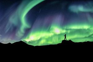 Hombre caminando en la montaña con explosión de auroras boreales foto