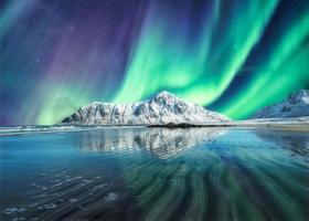 Aurora boreal, auroras boreales arriba en la montaña nevada en la playa de Skagsanden en las islas Lofoten foto