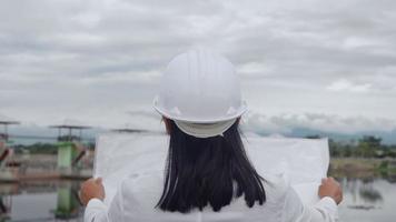 ingeniera con un casco blanco trabajando con una tableta digital y mirando hacia otro lado en el sitio de construcción de la presa para generar electricidad. video