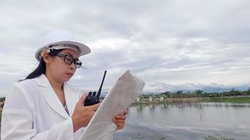 Female engineer in a white helmet working with a digital tablet and looking away at the dam construction site to generate electricity. video