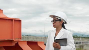 vrouwelijke ingenieur in een witte helm houdt een digitale tablet vast en gebruikt radiocommunicatie op de bouwplaats van de dam om elektriciteit op te wekken. schone energie en technologieconcepten. video