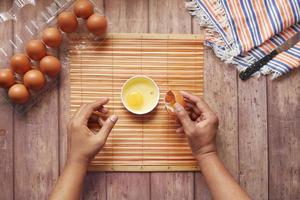 Man breaking egg and pouring into a small container on table photo