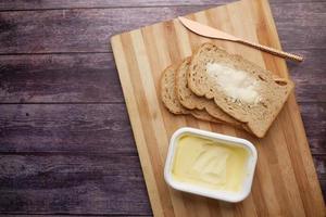 Slice of butter and whole meal bread on chopping board photo