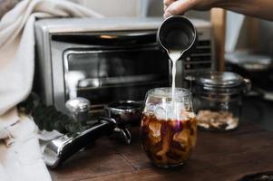 Barista pouring milk into a glass of iced coffee photo