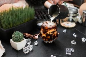 Barista pouring milk into a glass of iced coffee photo