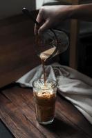 Barista pouring milk into a glass of iced coffee photo