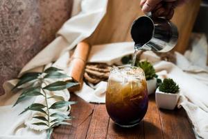 Barista pouring milk into a glass of iced coffee photo