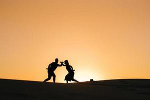 Siluetas de una joven pareja feliz sobre un fondo de naranja atardecer en el desierto de arena foto