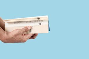 Man's hand holding and opening a thick book isolated on blue pastel color background photo