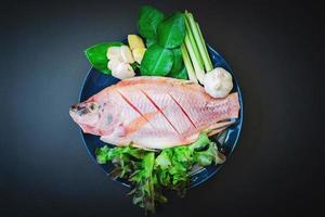 Pescado fresco y verduras en platos de cerámica sobre la mesa oscura preparada para cocinar foto