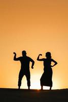 silhouettes of a happy young couple guy and girl on a background of orange sunset in the sand desert photo