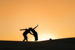 silhouettes of a happy young couple guy and girl on a background of orange sunset in the sand desert photo