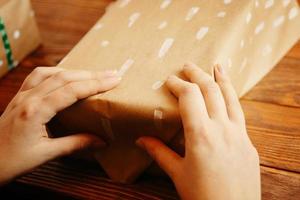 Close up of women's hands packing Christmas gift on wooden table. photo