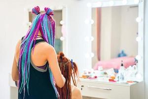 Hairdresser with colored afro braids weaves ginger dreadlocks. photo