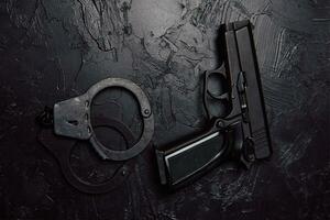 Gun and handcuffs on black textured table. photo