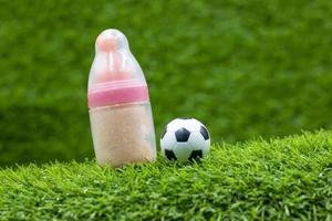 Soccer ball with pink bottle of milk are on green grass photo